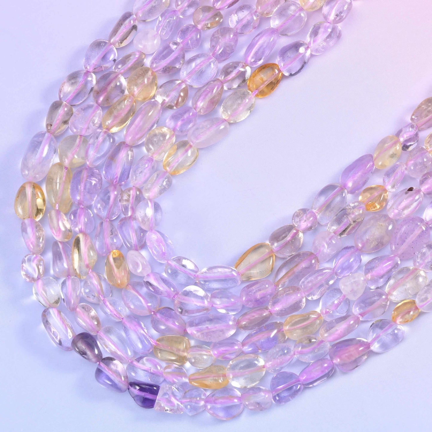 Soft lilac shading into honey gold within the same bead, showing the amethyst-and-citrine banding the stone is named for, tumbled into smooth translucent pebbles that glow when light passes through.