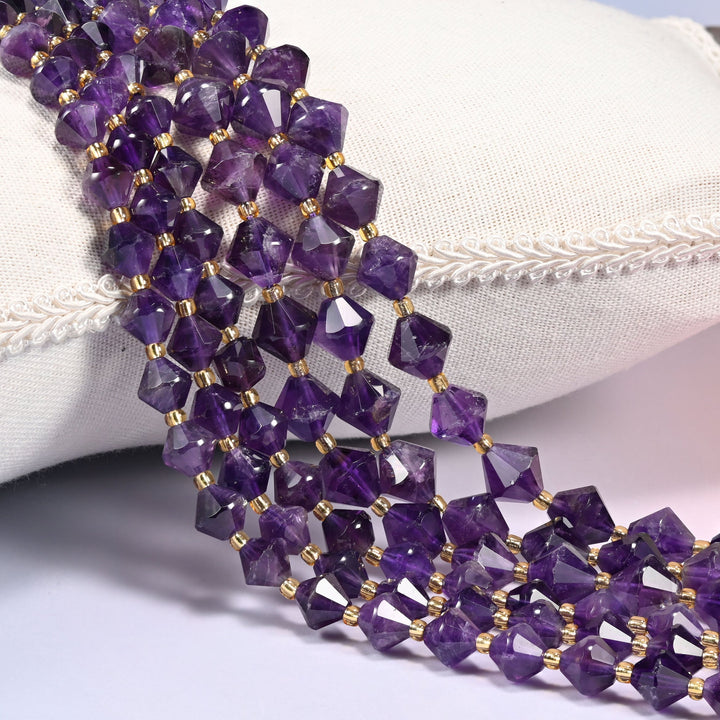 Dark amethyst faceted bicone beads over a white cushion, deep purple stone with gold seed spacers.