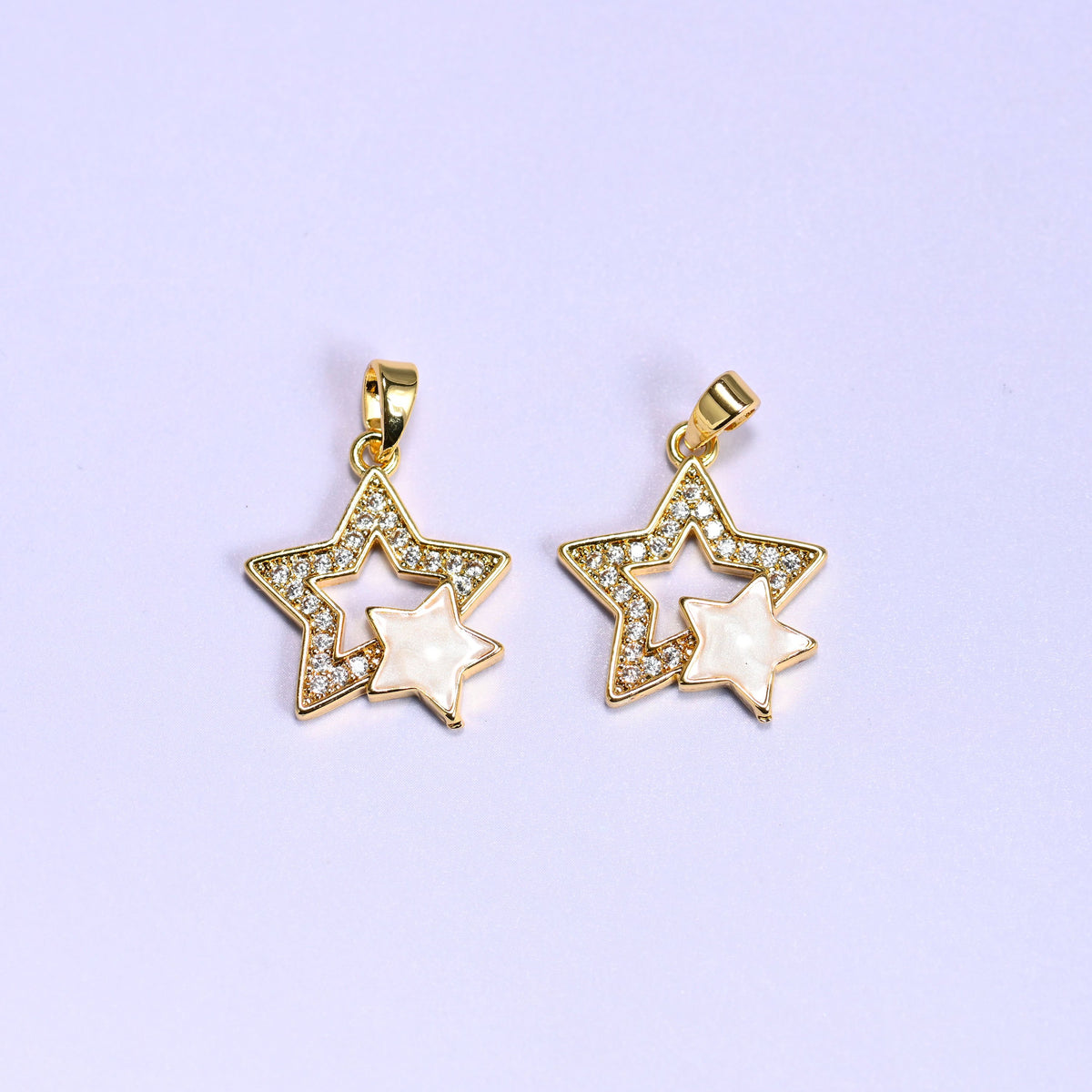 Double Stars Zirconia Charms in gold and white, two 18K gold plated pendants with clear zirconia pave outer stars and cream shell inner stars, shown side by side on a lilac background.