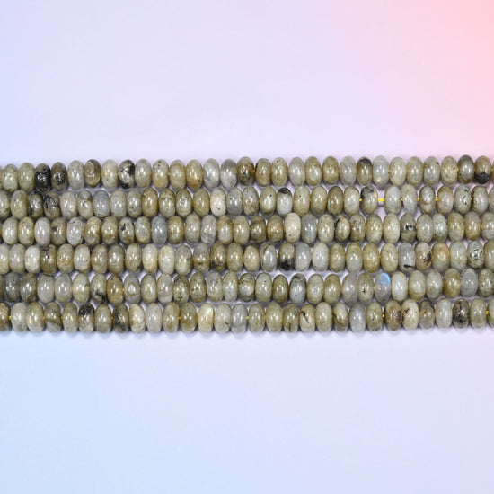 Overhead view of several rows of Grey Labradorite rondelle beads showing the soft grey and olive tones on a light lavender surface.
