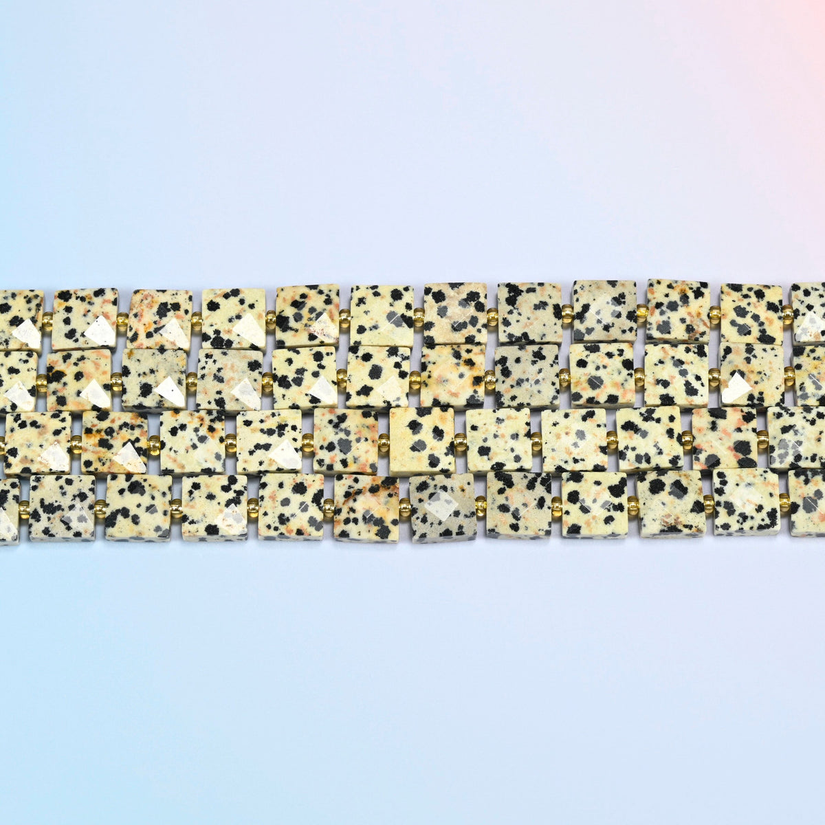 Several strands of dalmatian jasper faceted flat square beads laid in straight rows