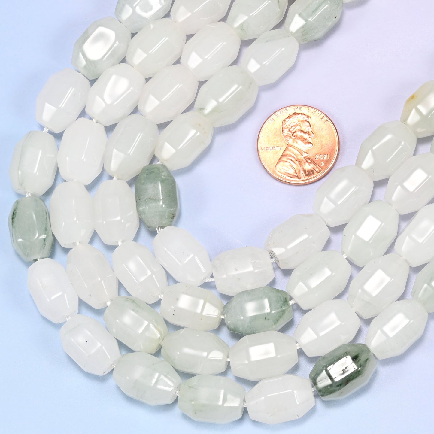 Circular coil of Tianshan Jade faceted barrel bead strands on a light background with a penny in the center for size comparison.