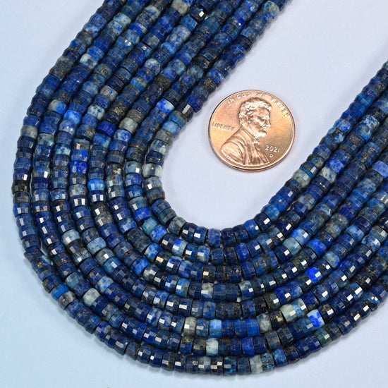 Close view of dark blue lapis faceted heishi disc strands curving beside a US penny for scale