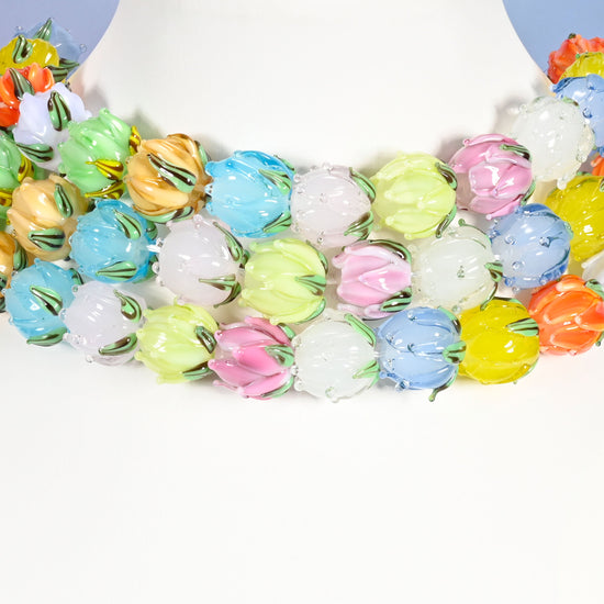 Multi-strand necklace of multicolor tulip bud lampwork glass beads laid on a white mannequin neck form against a lavender background.