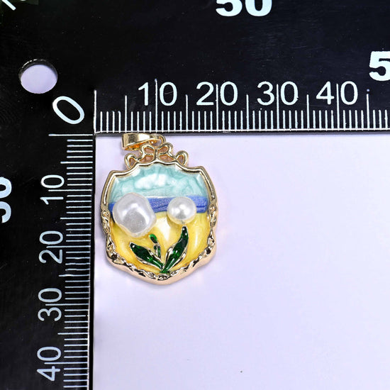 18K gold plated brass tulip charm pendant with a teal and yellow enamel garden scene, faux pearl tulip blooms, and green leaf details in an ornate shield frame.
