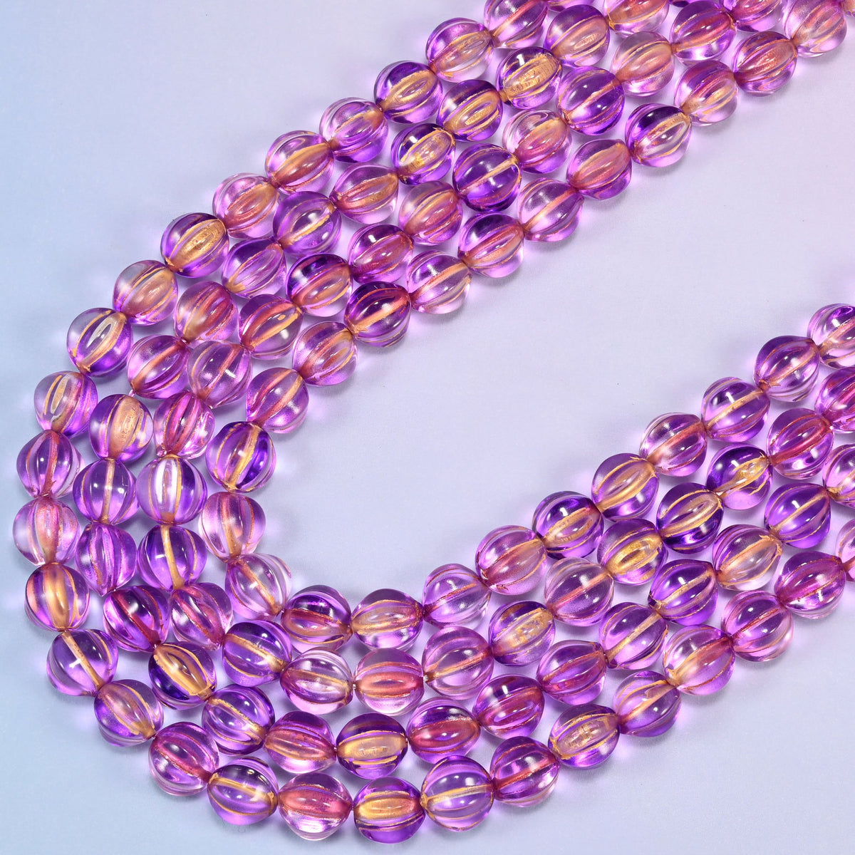 Purple gold pumpkin glass beads, several strands laid in a wide sweeping curve across the frame.