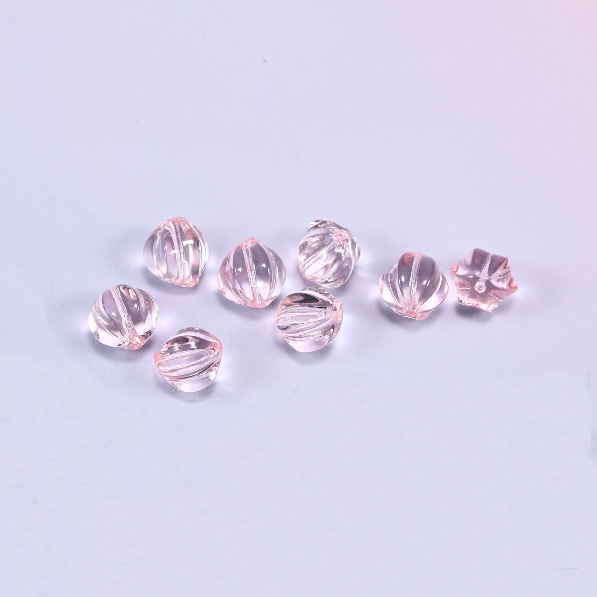 A scattered group of loose 8mm clear pink pumpkin glass beads, showing the melon ribs and the drill holes.