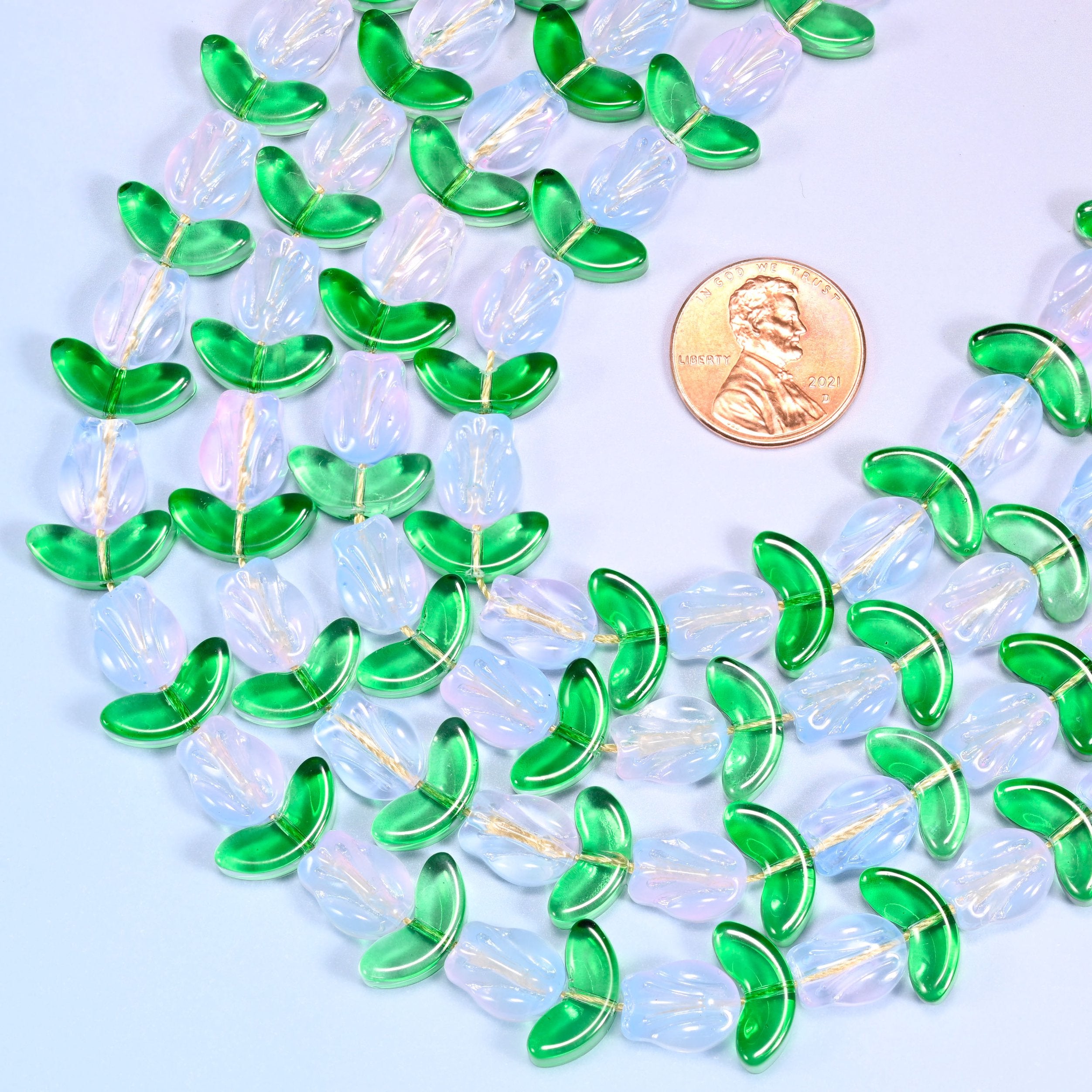 Wide view of a circular coil of tulip and leaf glass bead strands on a lavender background with a penny in the center for size comparison.