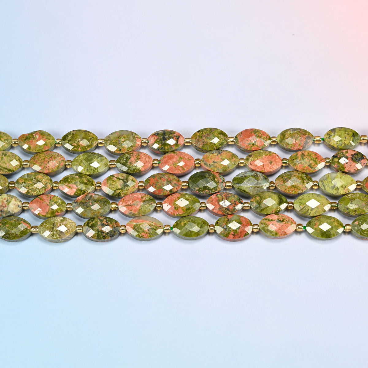 Several strands of unakite faceted flat oval beads laid in straight rows with gold seed bead spacers