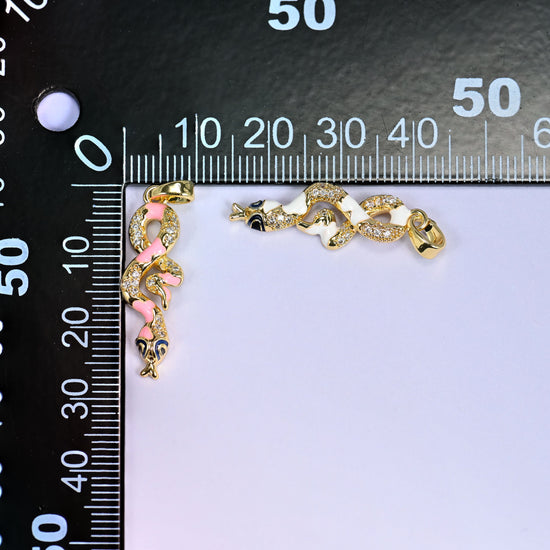 Pink and white Enamel Snake Zirconia Charms placed on a black millimeter ruler, one upright and one horizontal, for size reference.