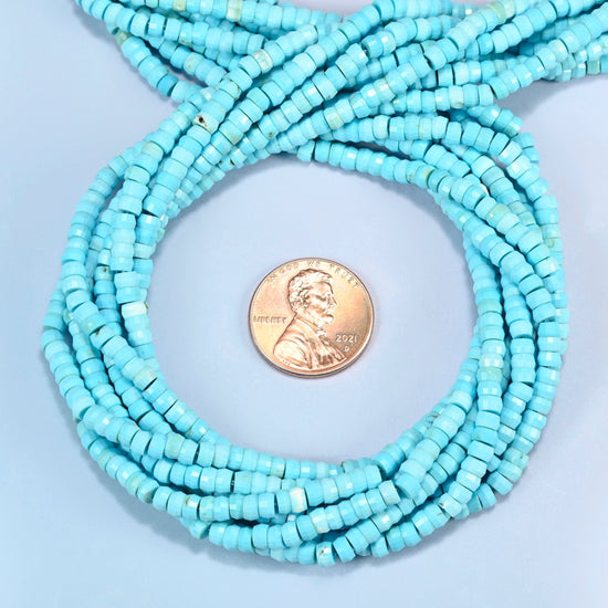 Dyed blue howlite faceted heishi disc beads 2x4mm coiled in a loop around a US penny for scale, close-up of the faceted disc shape