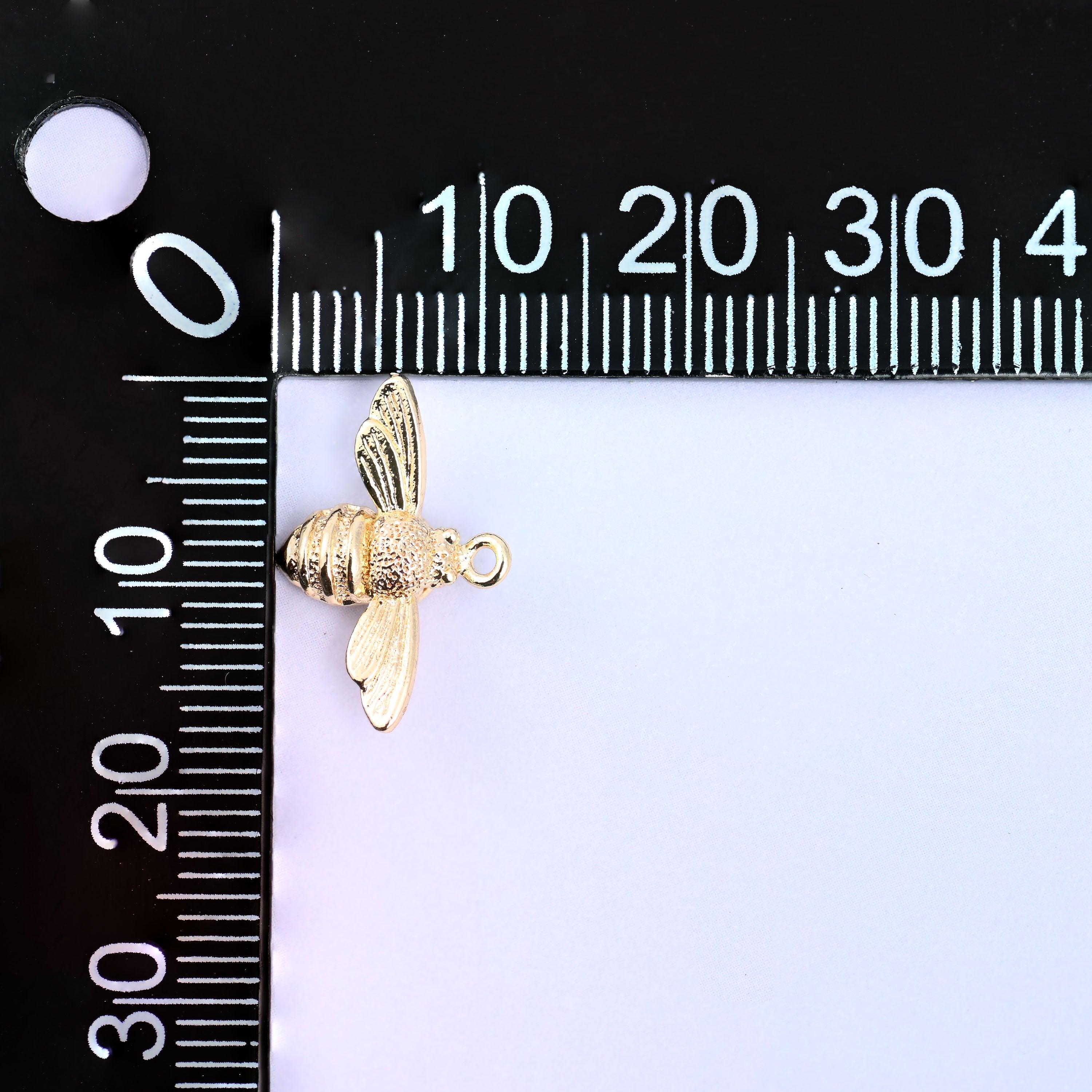 Small gold charms bee on a millimeter ruler showing the 11.7mm body height