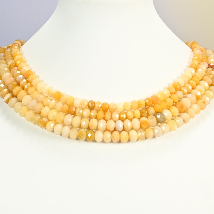 Gold silk jade beads shown on a white neck display, four faceted rondelle strands layered close to the neckline
