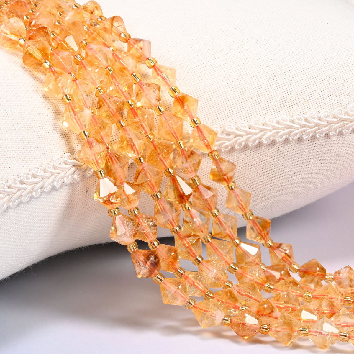 Citrine bicone beads laid out on the diagonal in several rows, warm translucent golden orange, a gold-tone spacer between every bead.