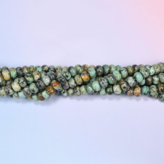 Bundled coil of African Howlite rondelle beads on a lavender background with a penny placed at the center for scale.