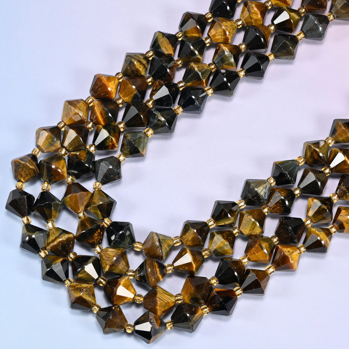 10mm Iron Tiger Eye faceted bicone beads arranged in a loose curved strand on a light lavender background.