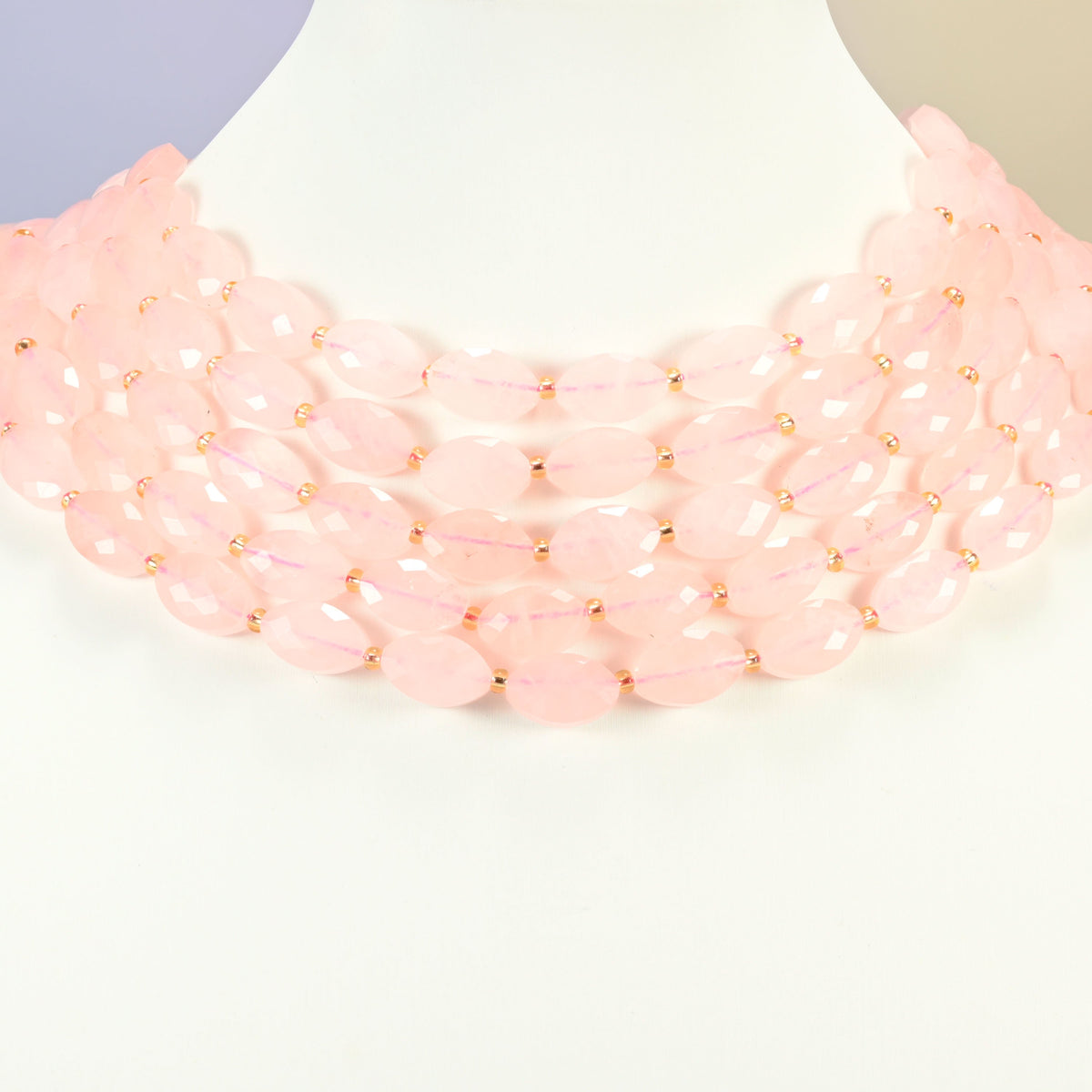 Rose quartz faceted flat oval strands arranged as a layered collar on a white display bust, light pink beads across the neck