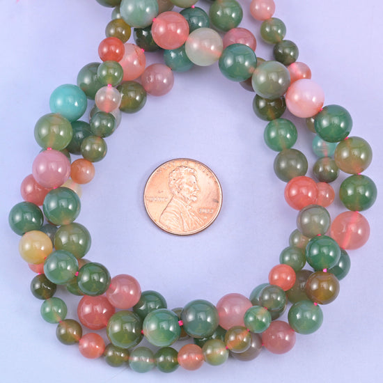 Green Yanyuan Agate round beads coiled around a US penny, larger rounds showing the full green to coral colour run