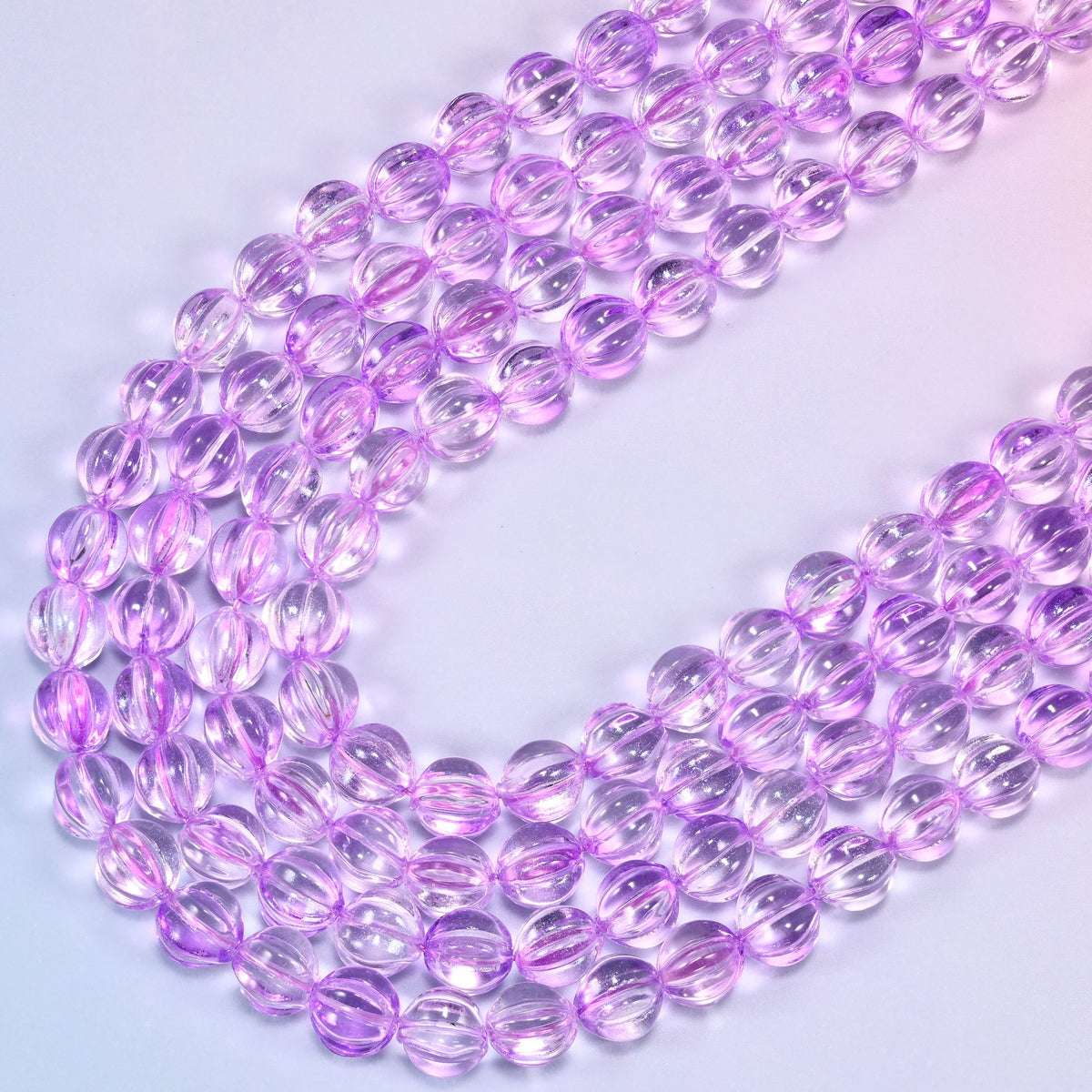 Clear purple pumpkin glass beads, several strands laid in a wide sweeping curve across the frame.