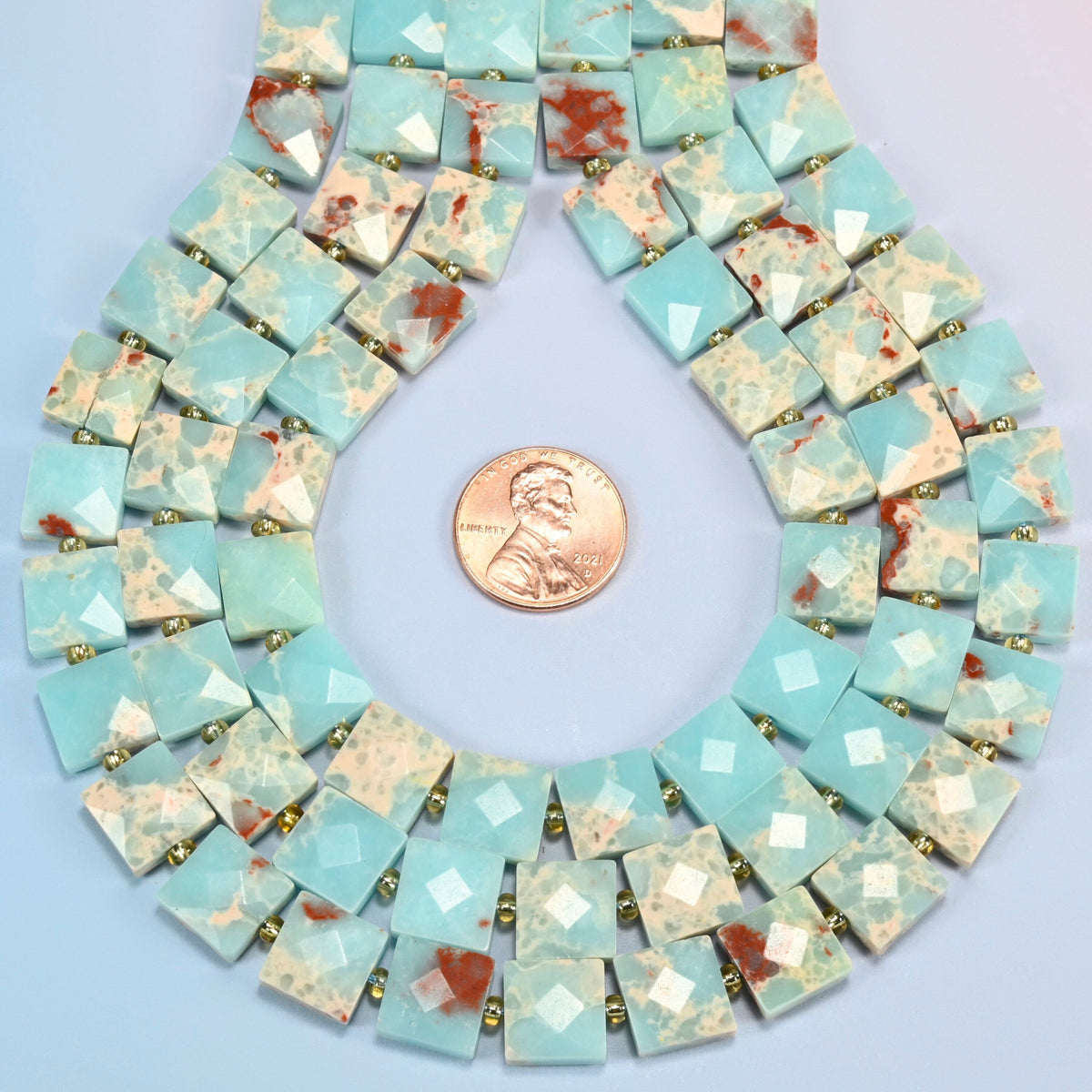 Dyed blue Shoushan stone faceted flat square strands formed into a teardrop loop around a US penny for scale