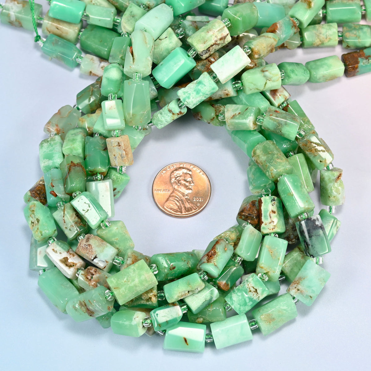Australian jade faceted tube beads 7x9-8x12mm coiled in a loop around a US penny for scale, close-up of the faceted tube shape