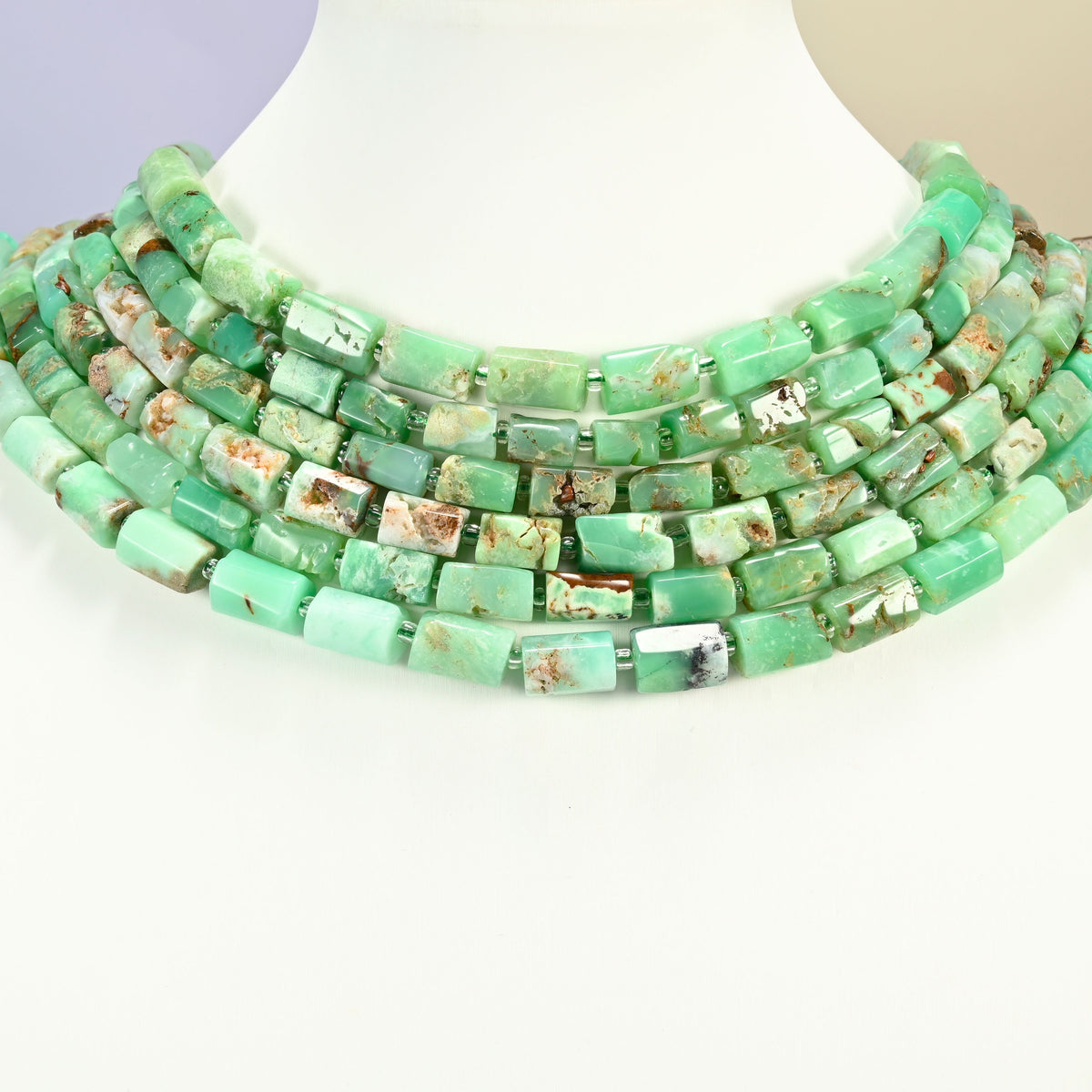 Australian jade faceted tube strands arranged as a layered collar on a white display bust, mint and apple green beads across the neck