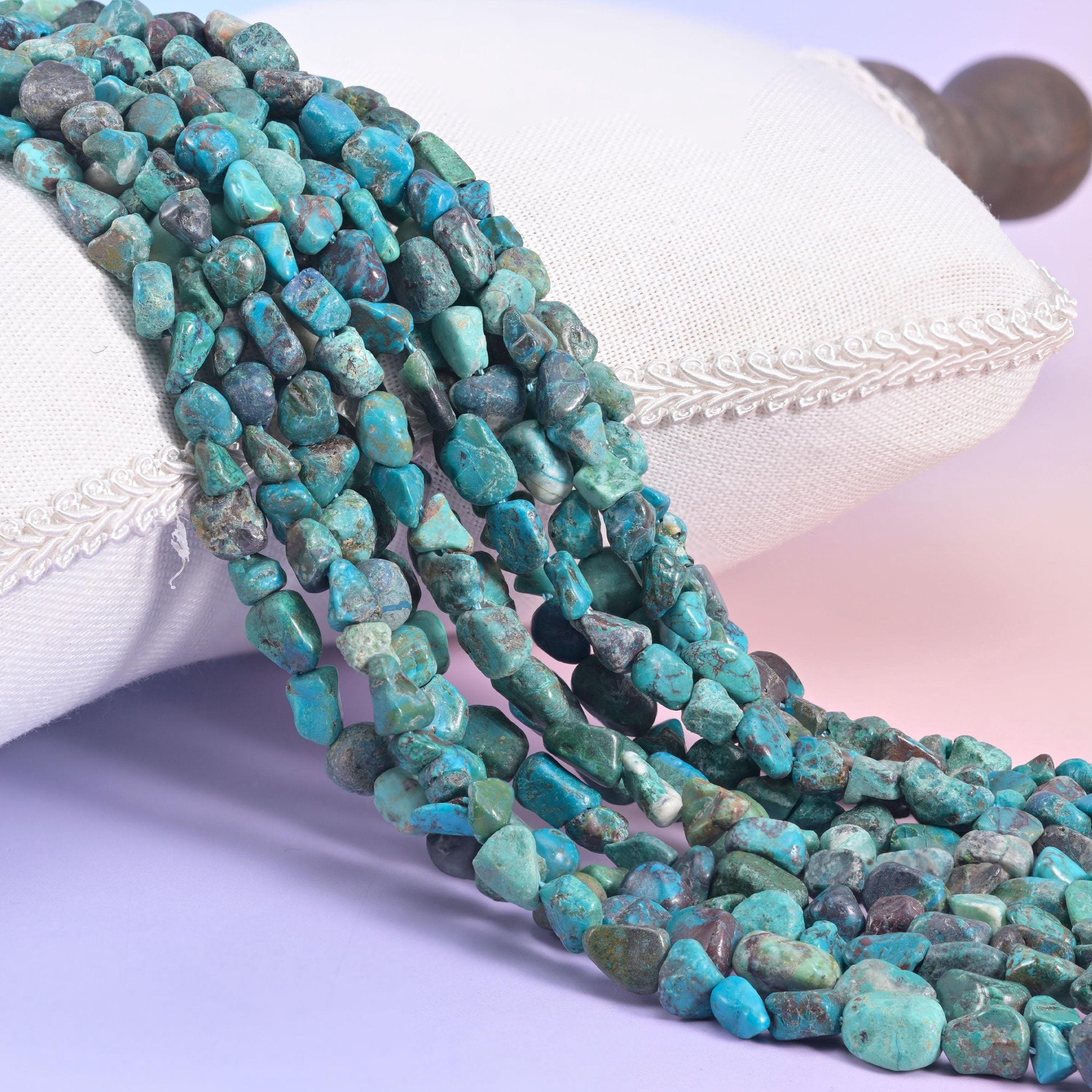 Turquoise nugget strands spilling over a white cushion, teal beads webbed with dark brown matrix