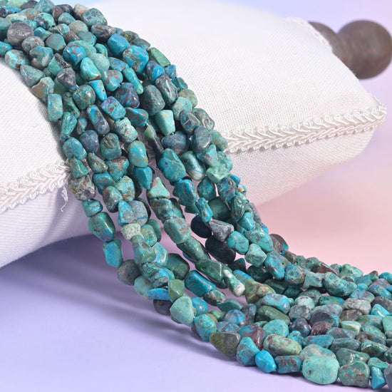 Turquoise nugget strands spilling over a white cushion, teal beads webbed with dark brown matrix