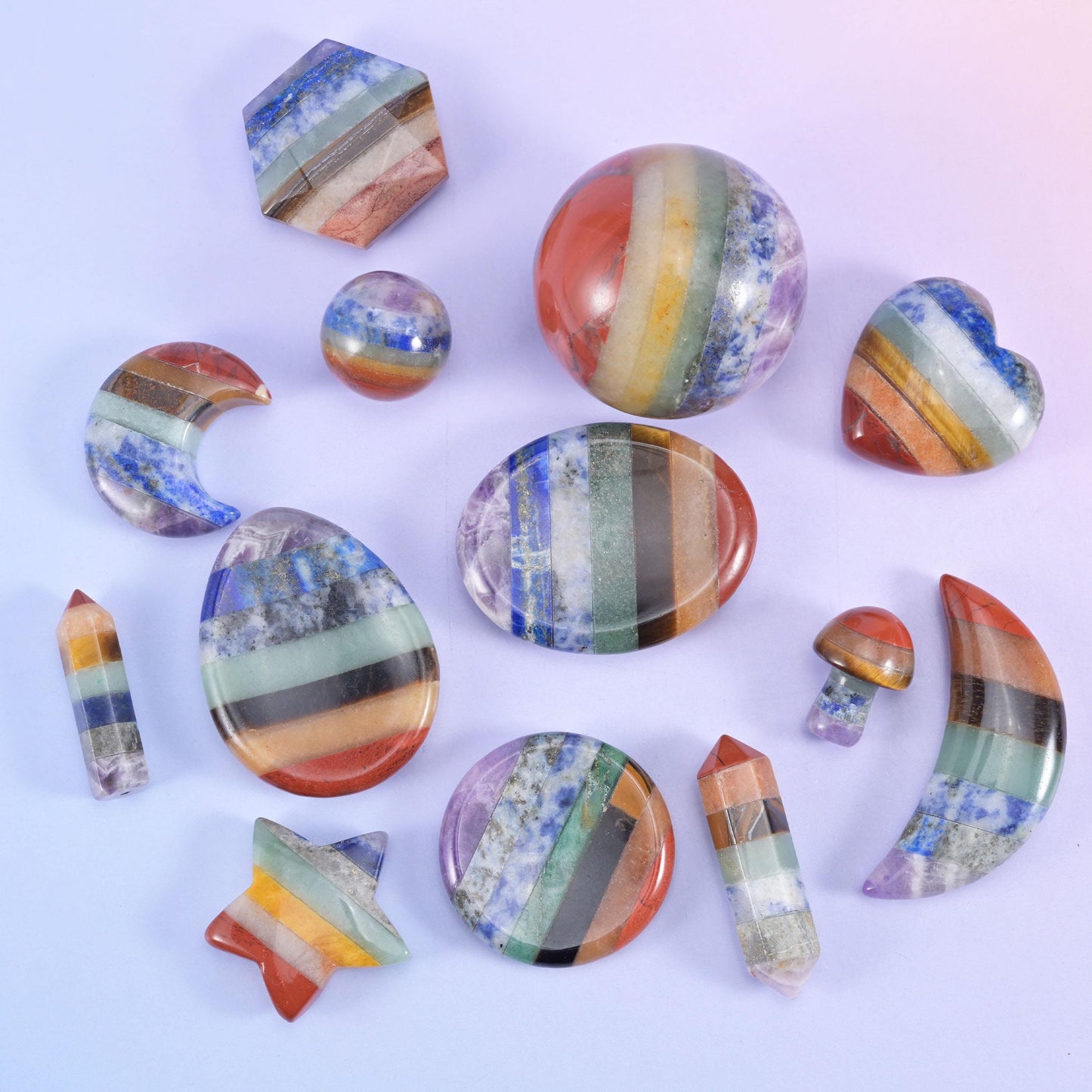 Assorted rainbow banded stone carvings including star, hexagon, sphere, coin and point shapes arranged on a pale lilac background