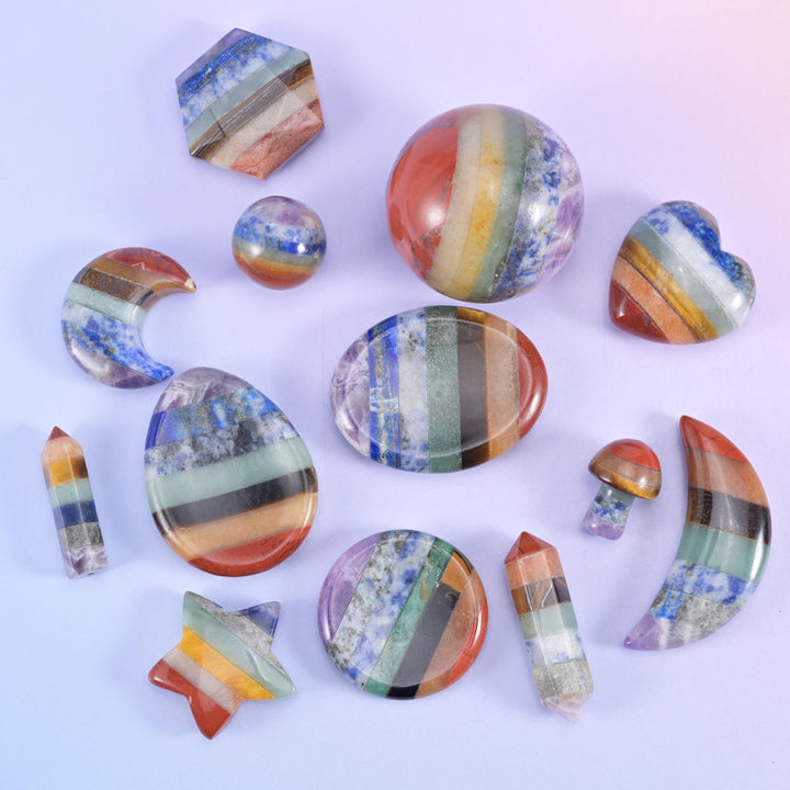 Assorted rainbow banded stone carvings including star, hexagon, sphere, coin and point shapes arranged on a pale lilac background
