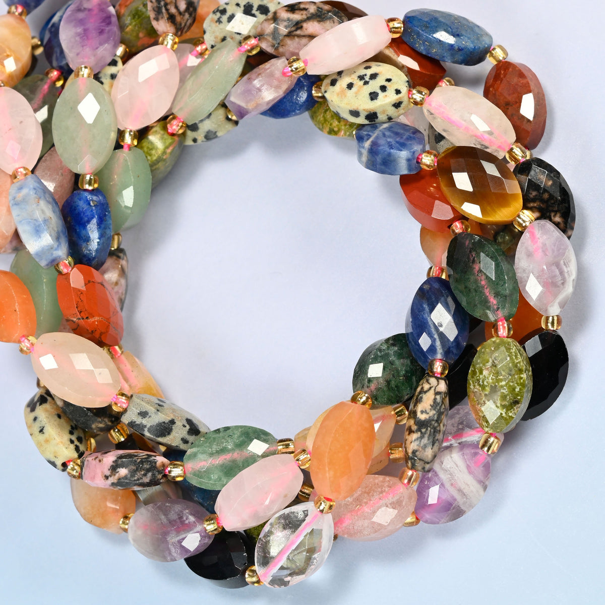 Assorted gemstone faceted flat oval beads coiled into overlapping loops, whole strands of multicolor stones