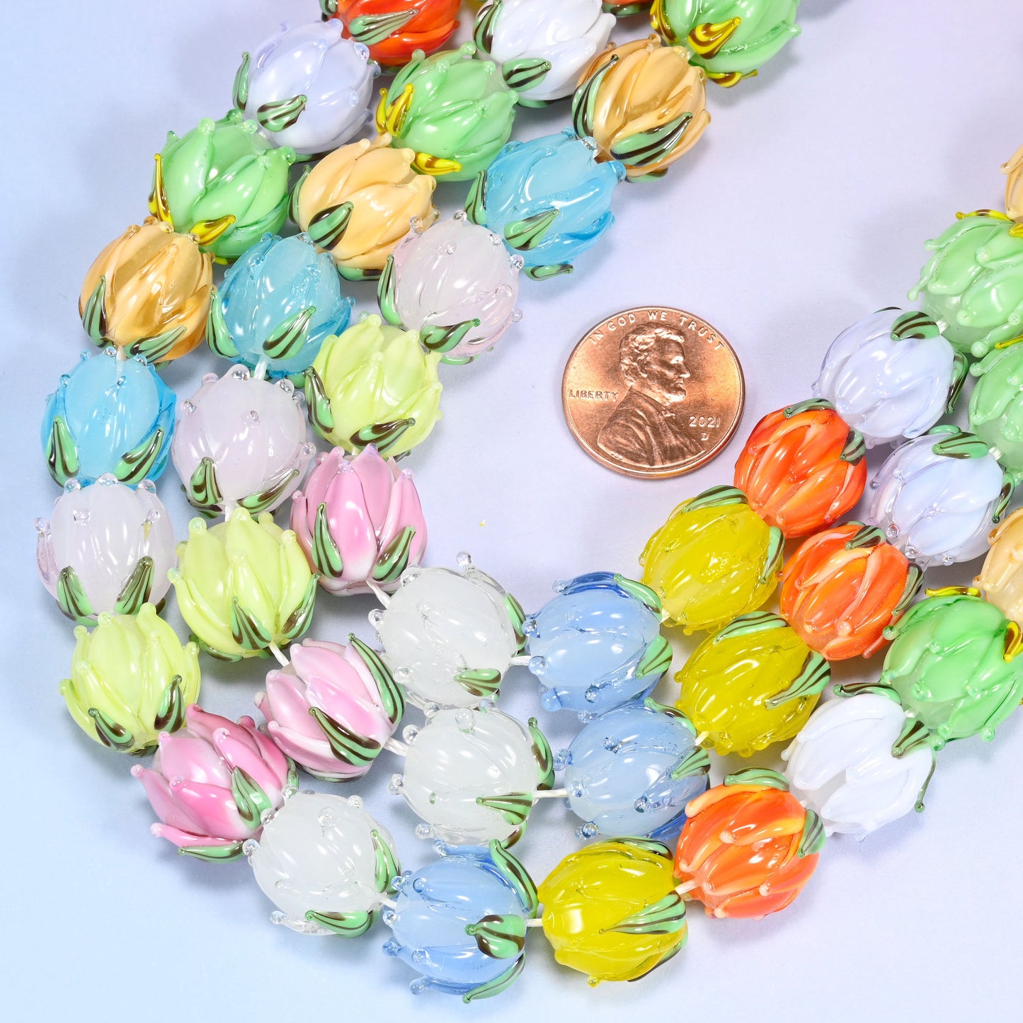 Close-up of a circular coil of multicolor tulip bud lampwork glass beads on a light lavender background.