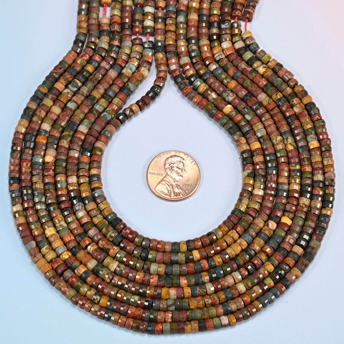 Red howlite faceted heishi disc strands formed into a teardrop loop around a US penny for scale