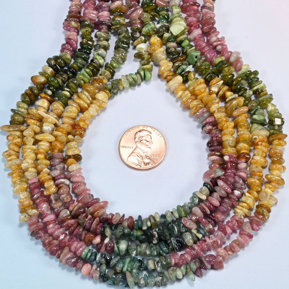 Multicolor tourmaline chip strands formed into a teardrop loop around a US penny for scale