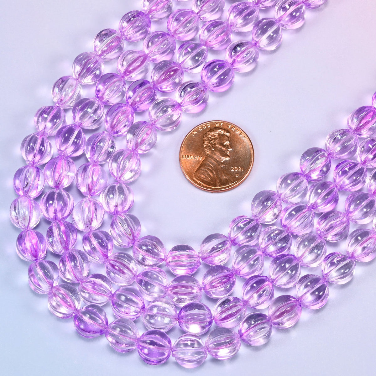 Clear purple pumpkin glass beads coiled loosely, shown with a US penny resting on the strands for scale.
