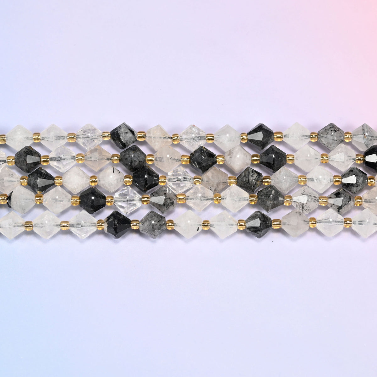 Black rutilated quartz bicone beads in straight rows, seen close up, each bead cut to two points meeting at a wide center, needles visible inside the quartz.