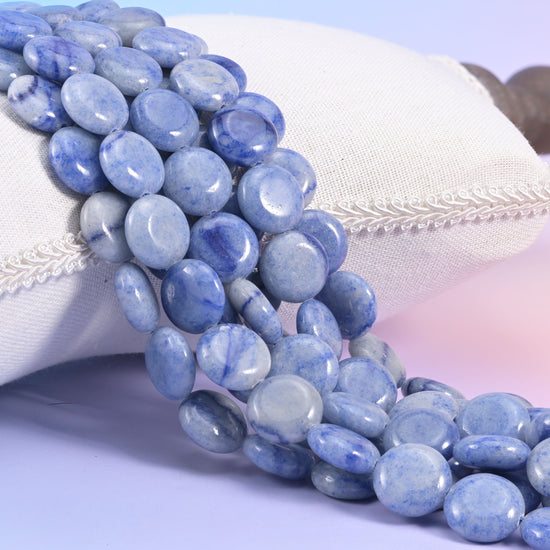 Blue aventurine coin strands resting against a cream linen cushion, periwinkle and pale grey 15mm discs on lilac