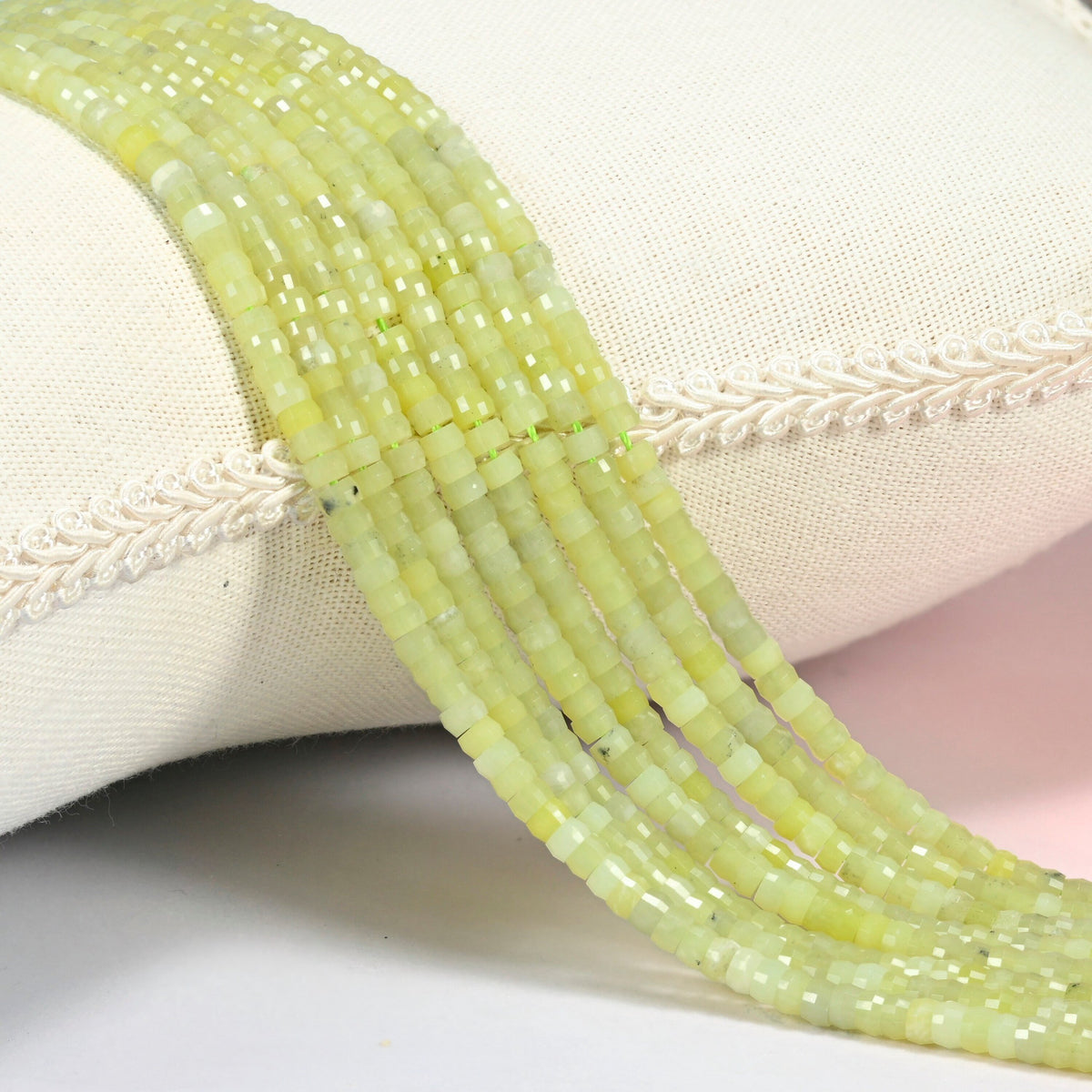 Lemon Jade faceted heishi disc beads 2x4mm, several strands draped over a white cushion