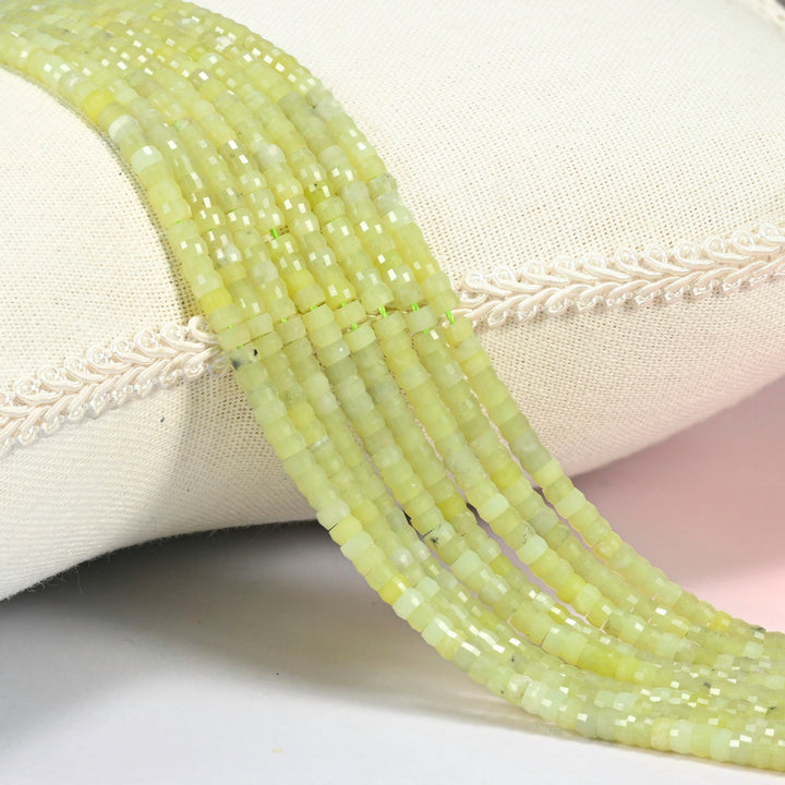 Lemon Jade faceted heishi disc beads 2x4mm, several strands draped over a white cushion