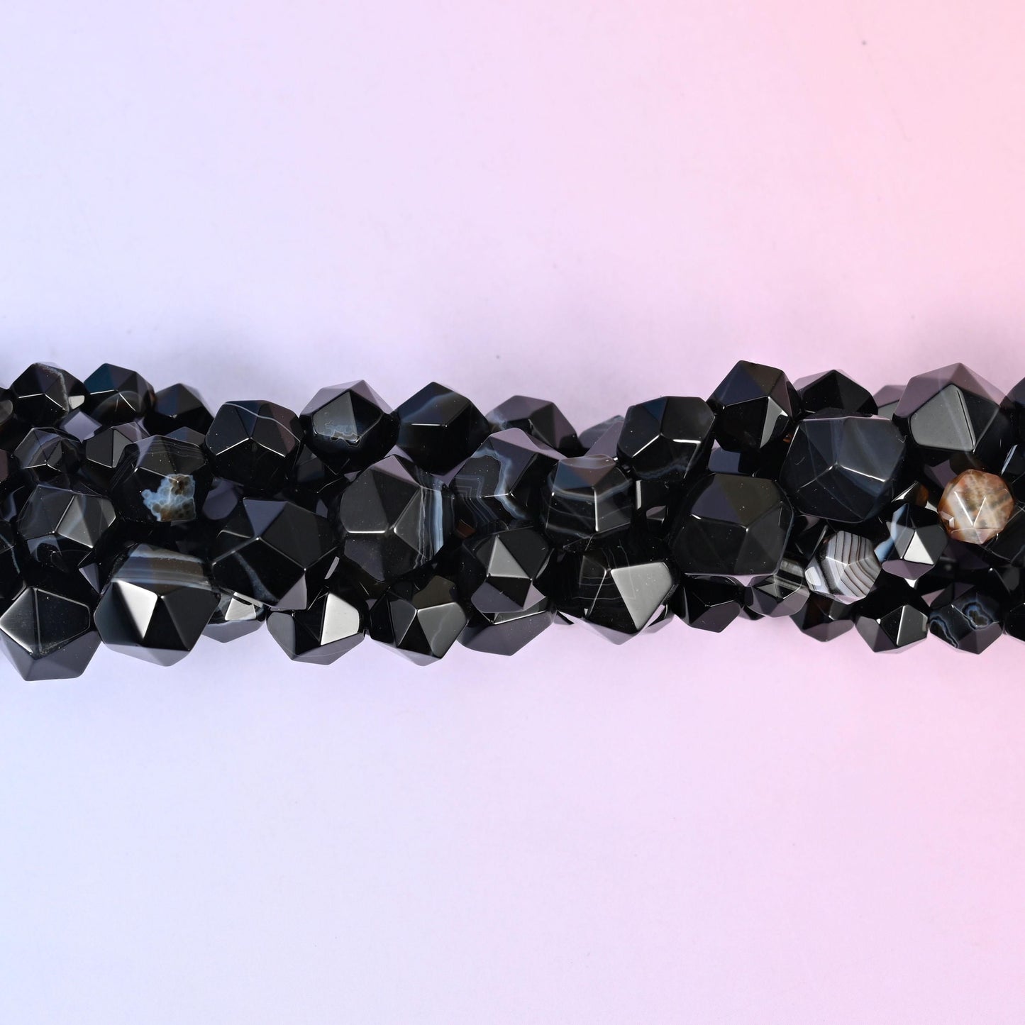 Glossy black rounds cut into a faceted diamond star, most of them crossed by a chalk-white stripe and a few carrying a caramel or grey band instead. Strong contrast in a small bead.
