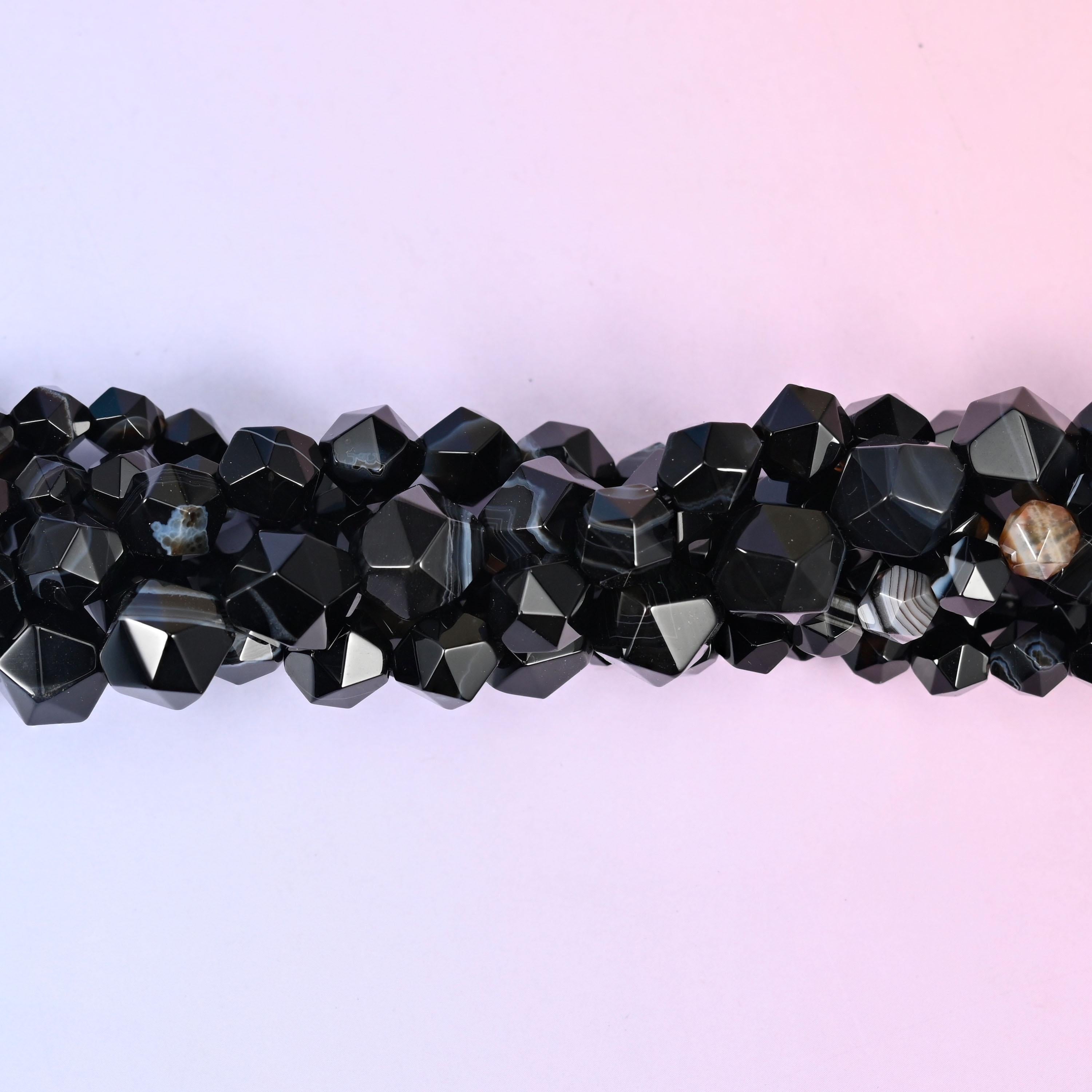 Glossy black rounds cut into a faceted diamond star, most of them crossed by a chalk-white stripe and a few carrying a caramel or grey band instead. Strong contrast in a small bead.