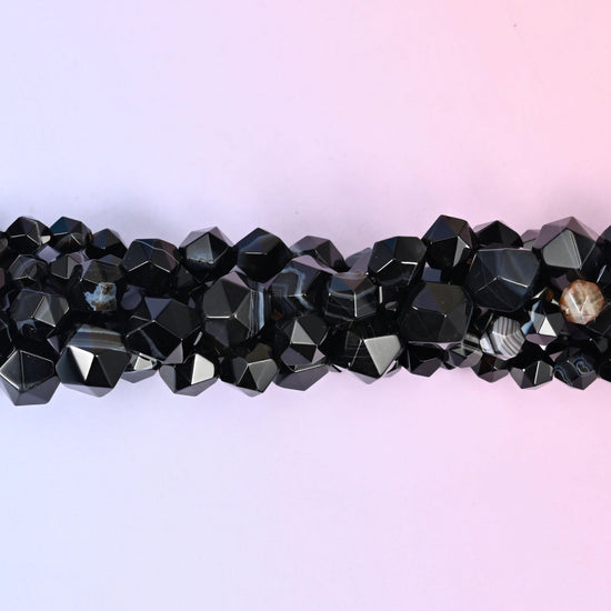 Glossy black rounds cut into a faceted diamond star, most of them crossed by a chalk-white stripe and a few carrying a caramel or grey band instead. Strong contrast in a small bead.