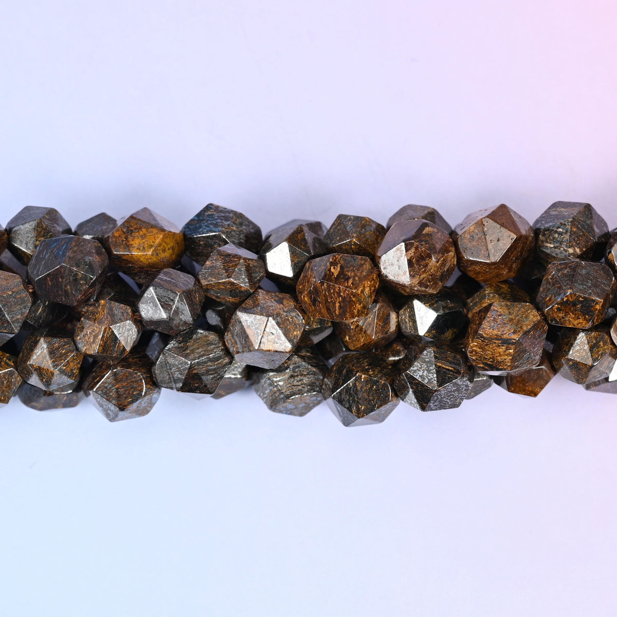 Warm bronze-brown rounds cut into sharp diamond star facets, each flat plane catching the light with a metallic shimmer over tan and cocoa mottling