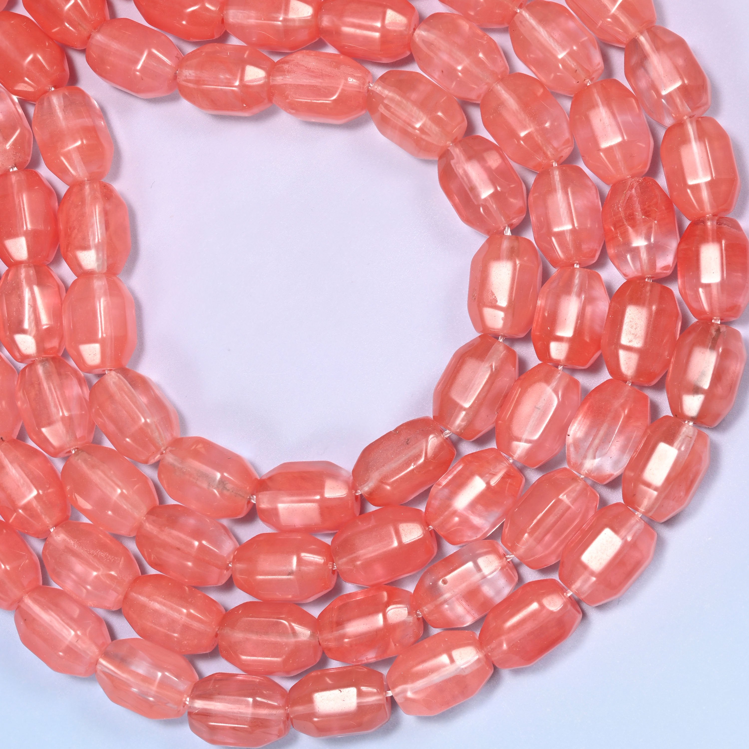 Close-up of a dense circular coil of coral pink faceted glass barrel beads, showing the translucent color depth.