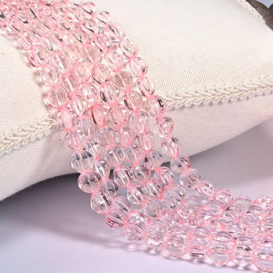Clear pink pumpkin glass beads, 8mm fluted melon rounds, several strands draped over a white cushion.