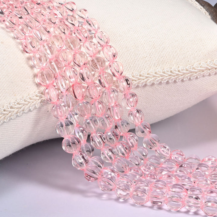 Clear pink pumpkin glass beads, 8mm fluted melon rounds, several strands draped over a white cushion.