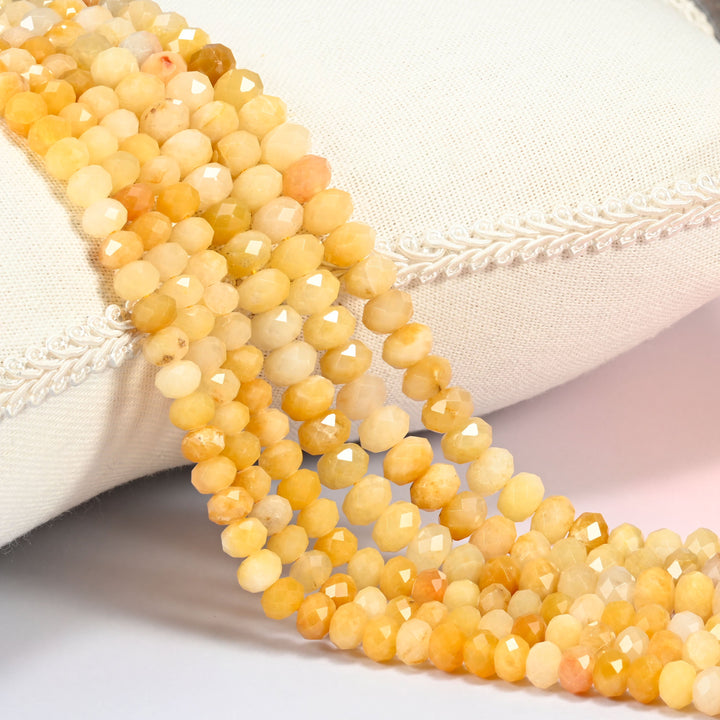 Gold silk jade faceted rondelle beads in light yellow and golden yellow, several strands draped over a cream cushion with braided trim
