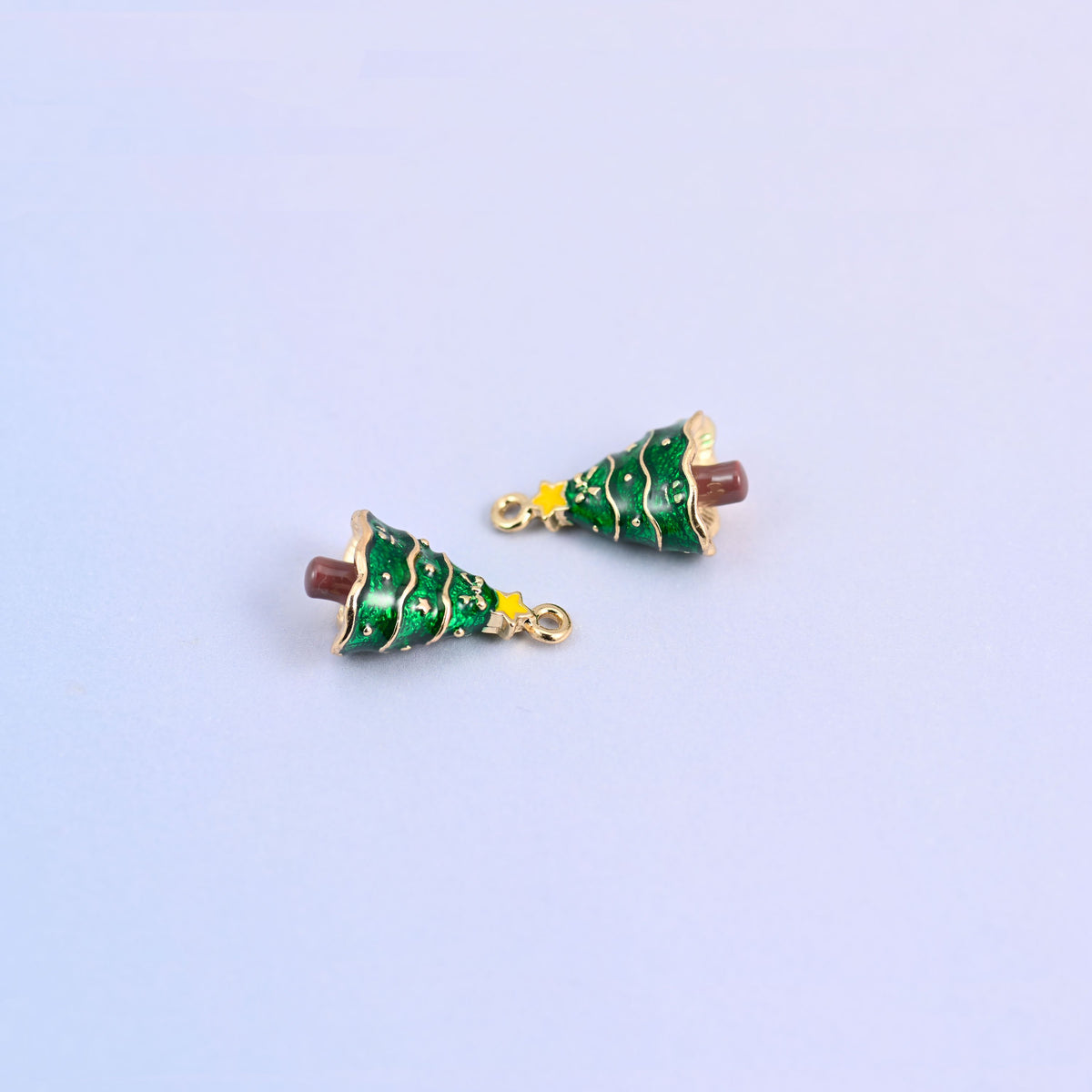 Two christmas tree charms lying at an angle, green enamel branches with fine gold garland lines.