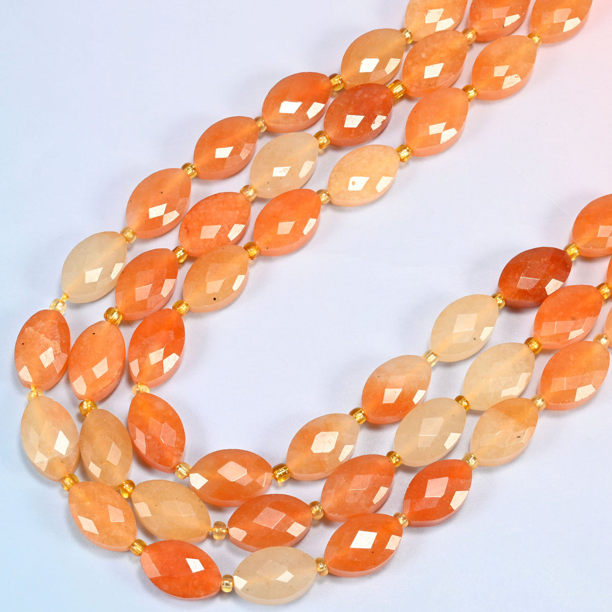 Red aventurine faceted flat oval beads in several strands curved into a wide U, peach to burnt orange stone