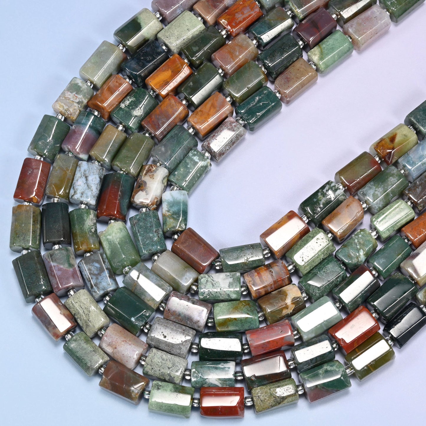 Close-up of faceted Indian Agate tube beads with clear glass spacer beads coiled in a circular arrangement on a lavender background.